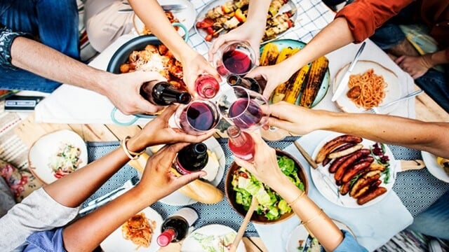 People toasting with wine glasses over a table filled with assorted foods